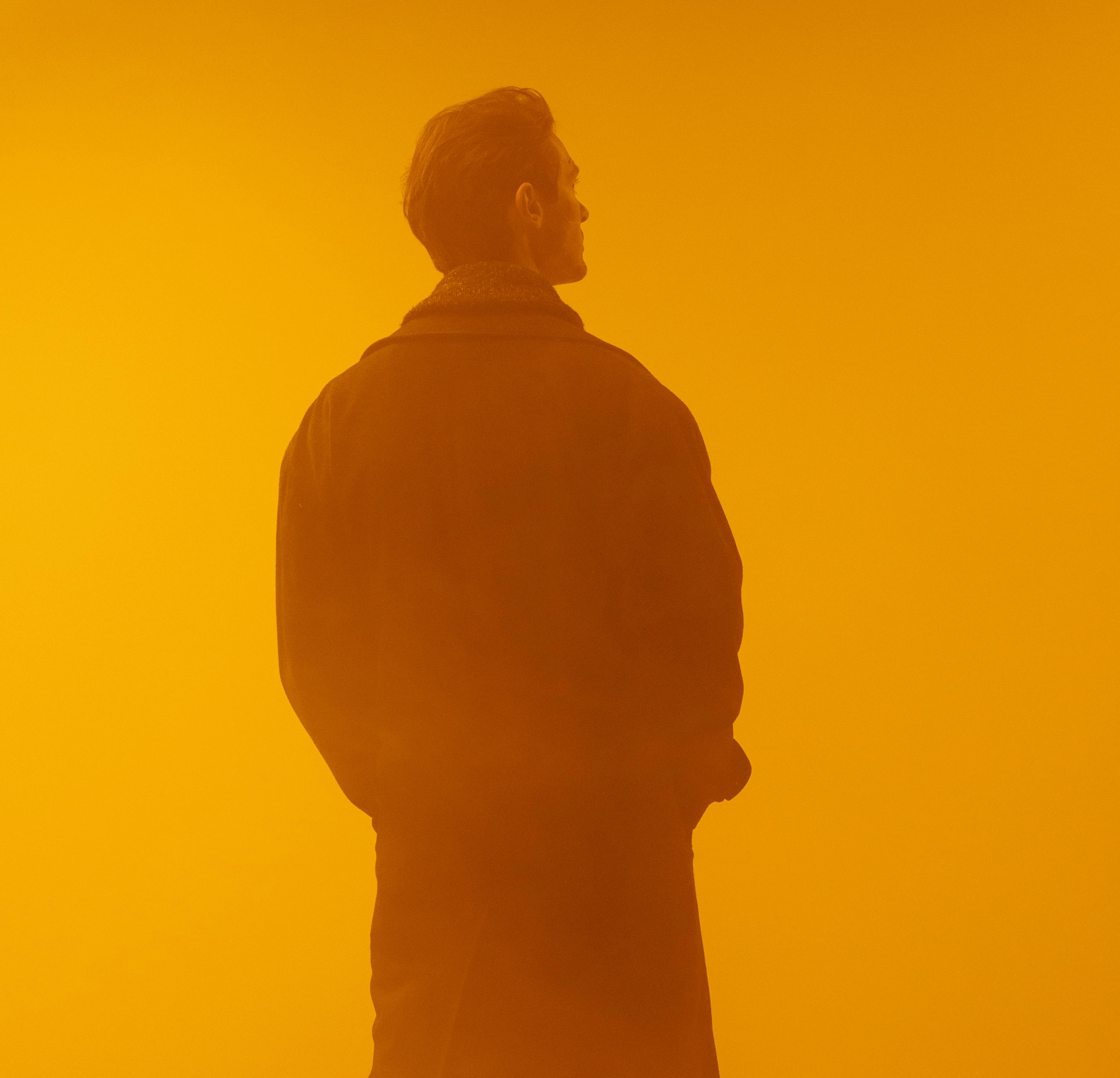 Man in a coat standing with his back turned in a foggy orange-lit environment